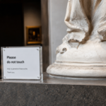 Deflecto A4 Magnetic Acrylic Block 30mm displaying a "please do not touch" sign beside a sculpture in a gallery
