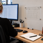 Deflecto A4 Wall Planner – Fixed Mount mounted above an office desk with a monitor and keyboard