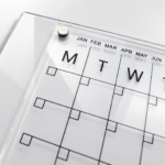 Close-up of the Deflecto A4 magnetic wall planner showing a corner magnet, month labels and day columns